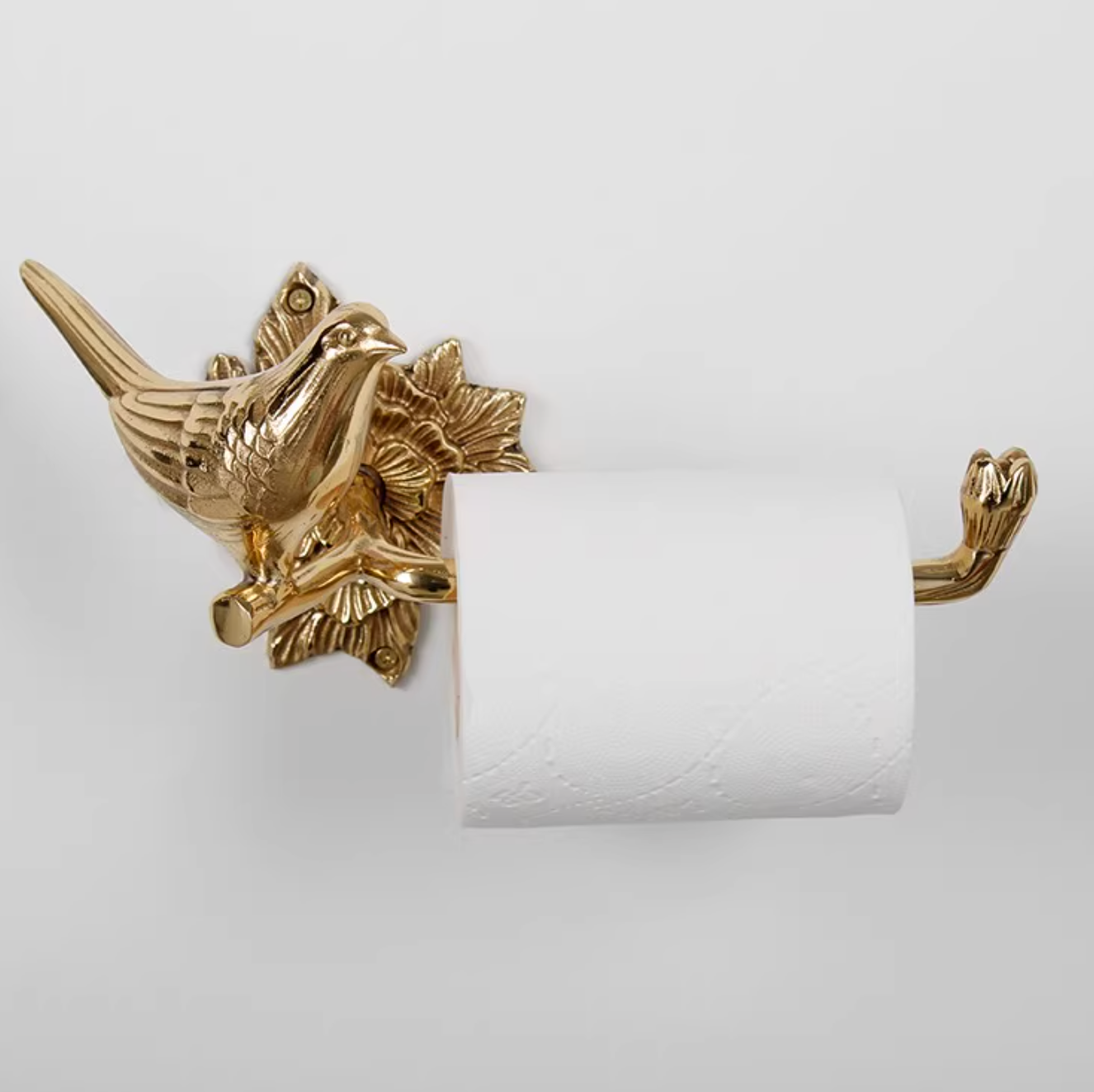 Gold brass bird toilet paper holder on white wall.
